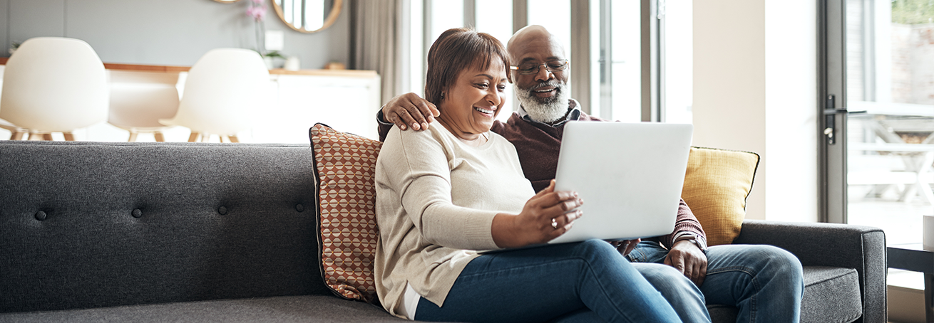 Couple sitting next to each other on the couch looking at their laptop.
