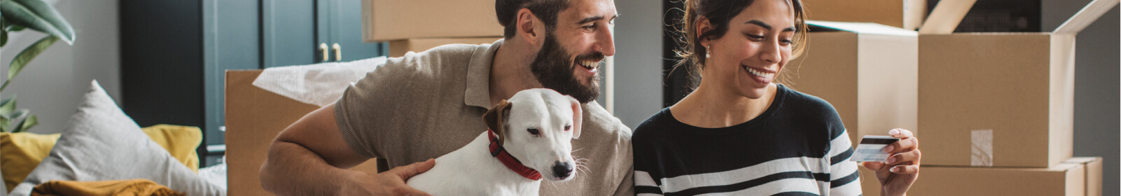 A couple and their dog sitting with moving boxes around them